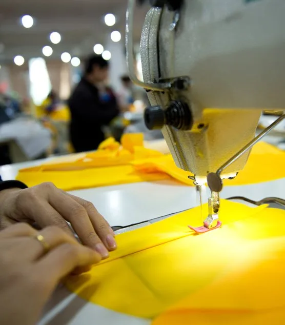 Costureira operando máquina de costura industrial sobre tecido amarelo na fábrica da VestCo