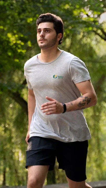 Homem correndo em parque vestindo camiseta cinza VestCo esportiva